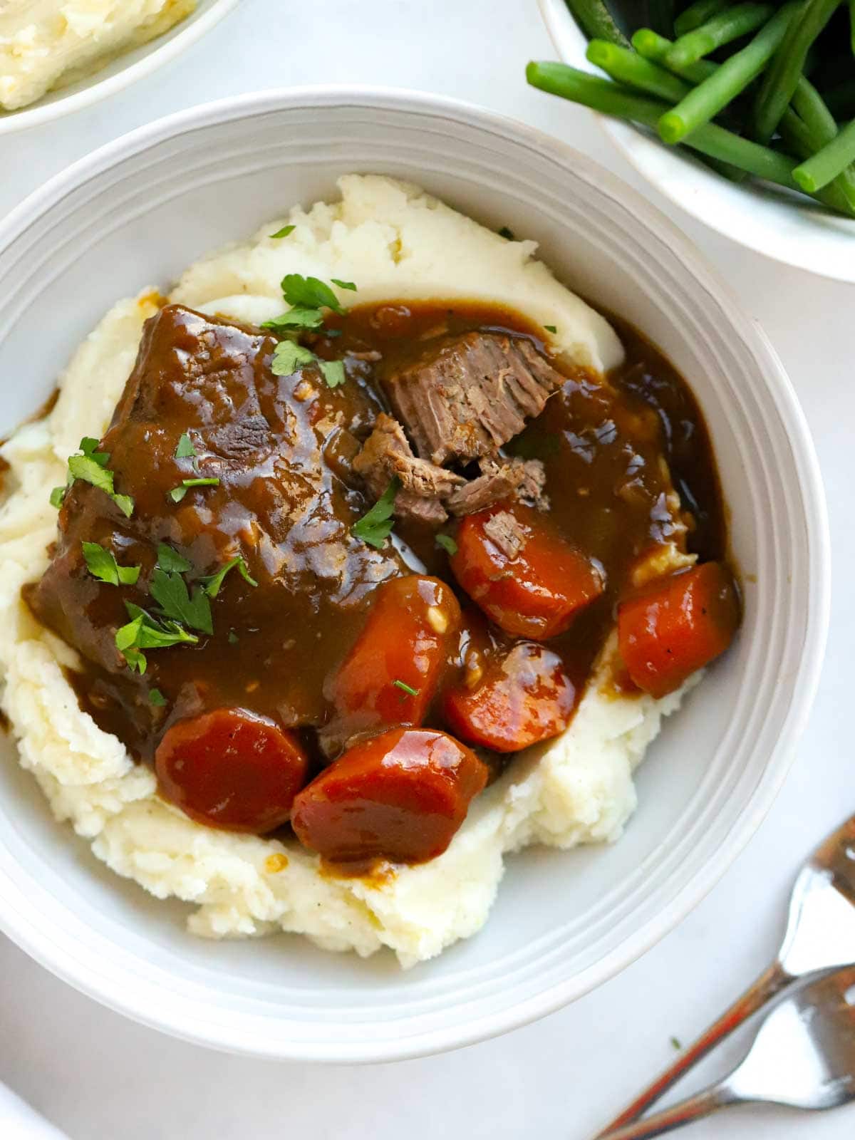 A bowl of homemade braised steak with carrots on a bed of mashed potato.