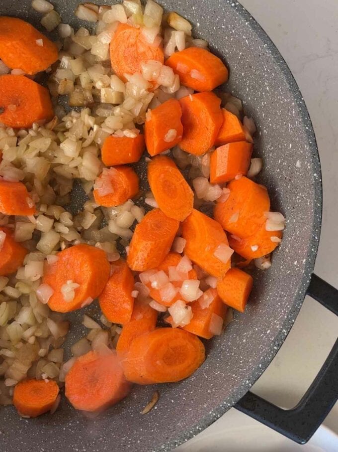 Carrots and onion frying in a pan for step 2 in the recipe for Tender Braised Steak.