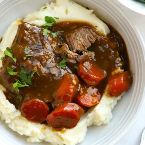 A plate filled with mashed potato and braised steak with carrots and a side of green beans.