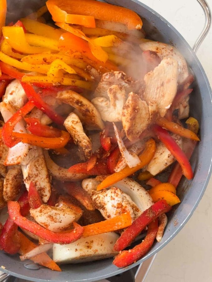 Chicken cooking in a pan with peppers for a chicken fajita pasta bake recipe. Step 1.