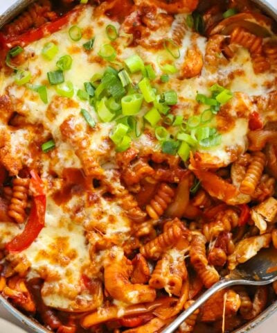 Big pan full of Chicken Fajita Pasta Bake with cheese and spring onion on top.