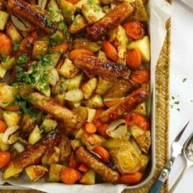 Tray filled with cooked sausages and vegetables for the recipe Sticky Sausage Tray Bake.