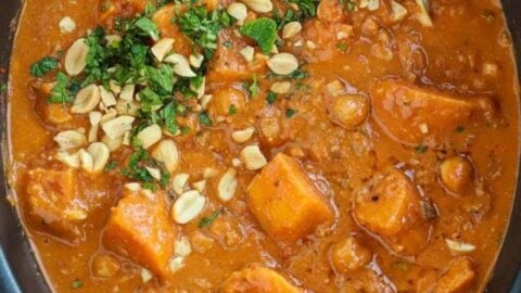 Sweet potato and peanut butter vegan stew in a slow cooker, garnished with peanuts and parsley.