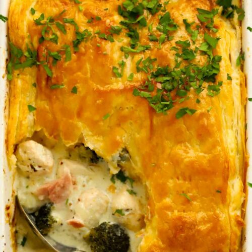 Chicken, broccoli and ham pie topped with a puff pastry crust, with a portion missing.