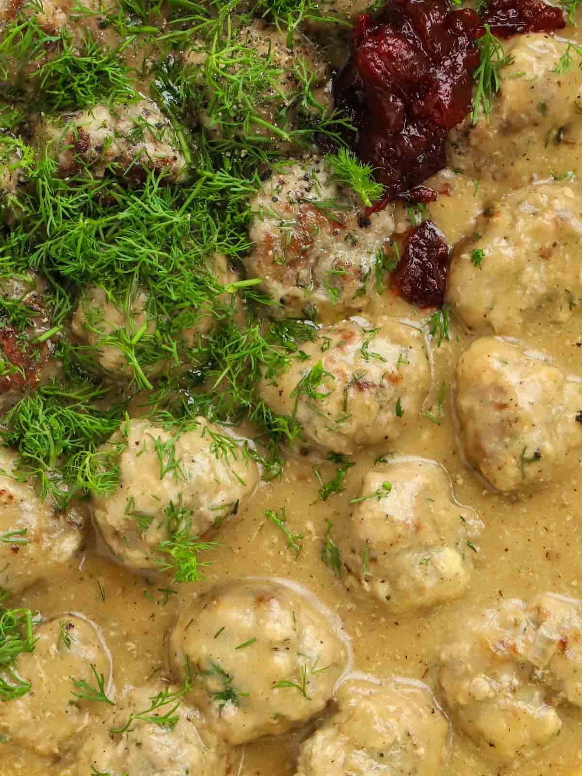 Close up of Swedish Meatballs in a creamy sauce with fresh dill and redcurrant jelly.