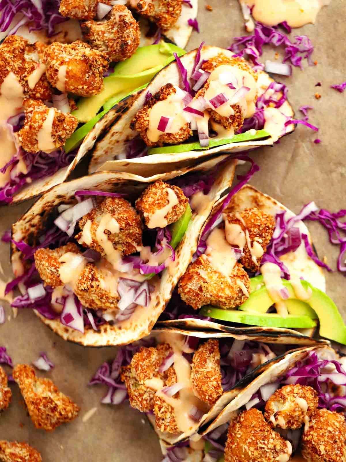 A row of Cauliflower Tacos stuff with salad, crispy cauliflower and topped with a sweet chilli mayo.