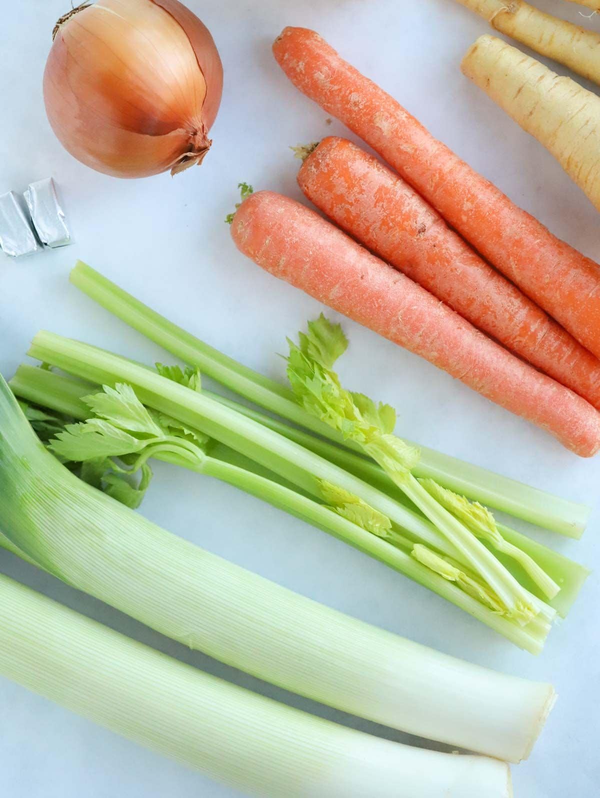 Ingredients for slow cooker vegetable soup laid on a counter. Carrots, leeks, onion, parsnip and celery.