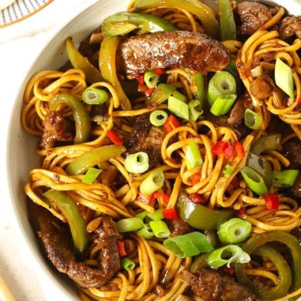 Close up of a big bowl of sticky beef stir fry with noodles, topped with spring onion and filled with veg.