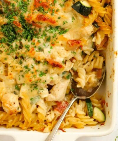 An oven proof dish filled with cooked Chicken and Bacon Pasta Bake, topped with cheese and parsley.