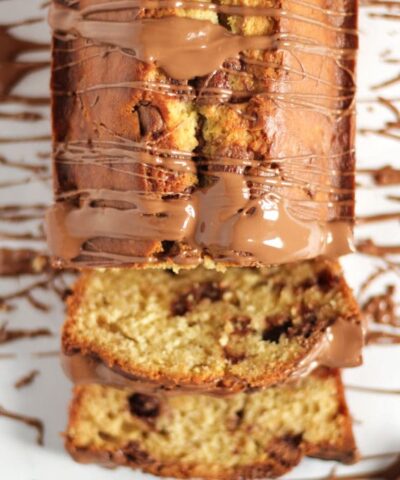 A loaf-shaped Banana Cake with chocolate chips and chocolate drizzled over the top. Sliced and ready to eat.
