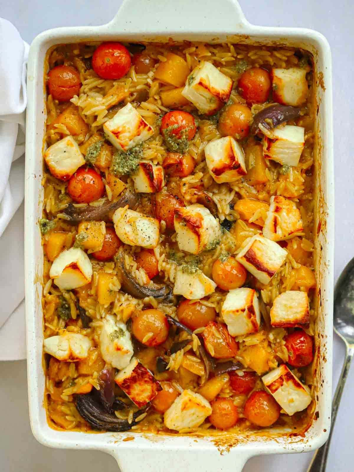 An oven dish filled with Butternut Squash and Halloumi Orzo Bake with cherry tomatoes.
