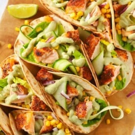 Easy salmon tacos recipe on a wooden board with cucumber and avocado dressing