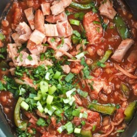 A slow cooker pan filled with cooked Campfire Stew and topped with spring onions.