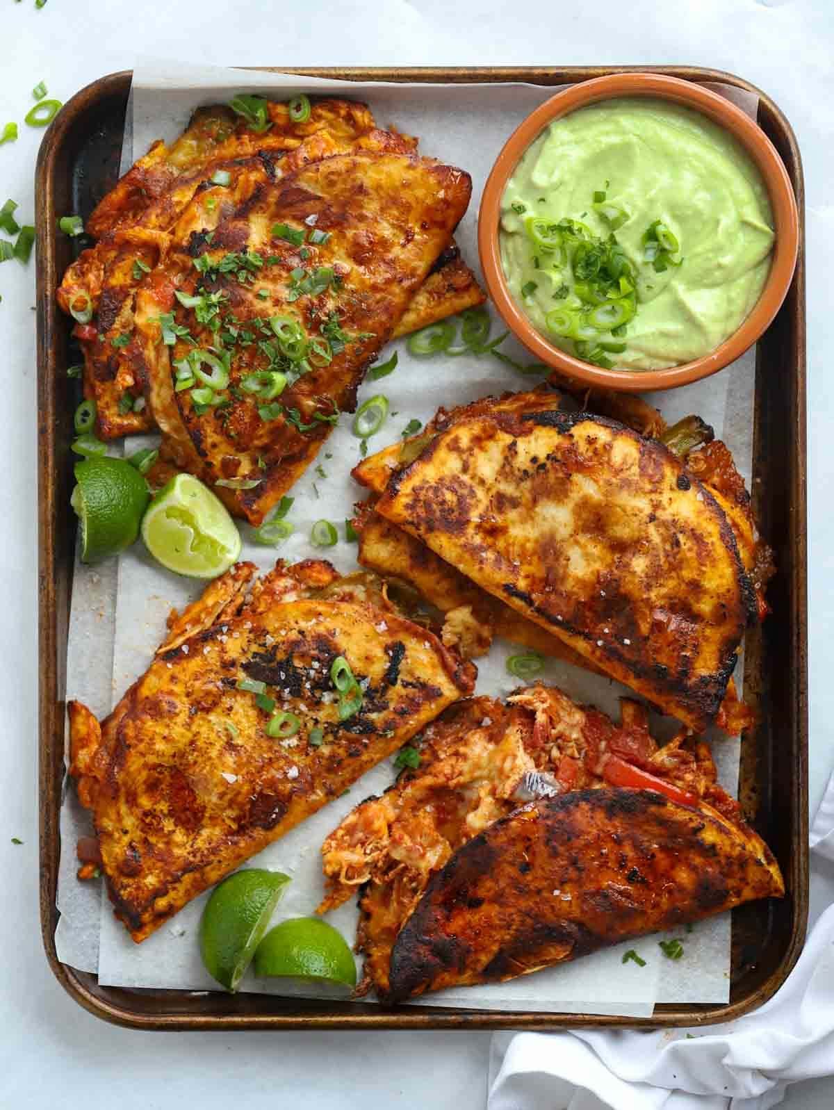 Fried chicken tacos in a tray with chicken and an avocado sauce.