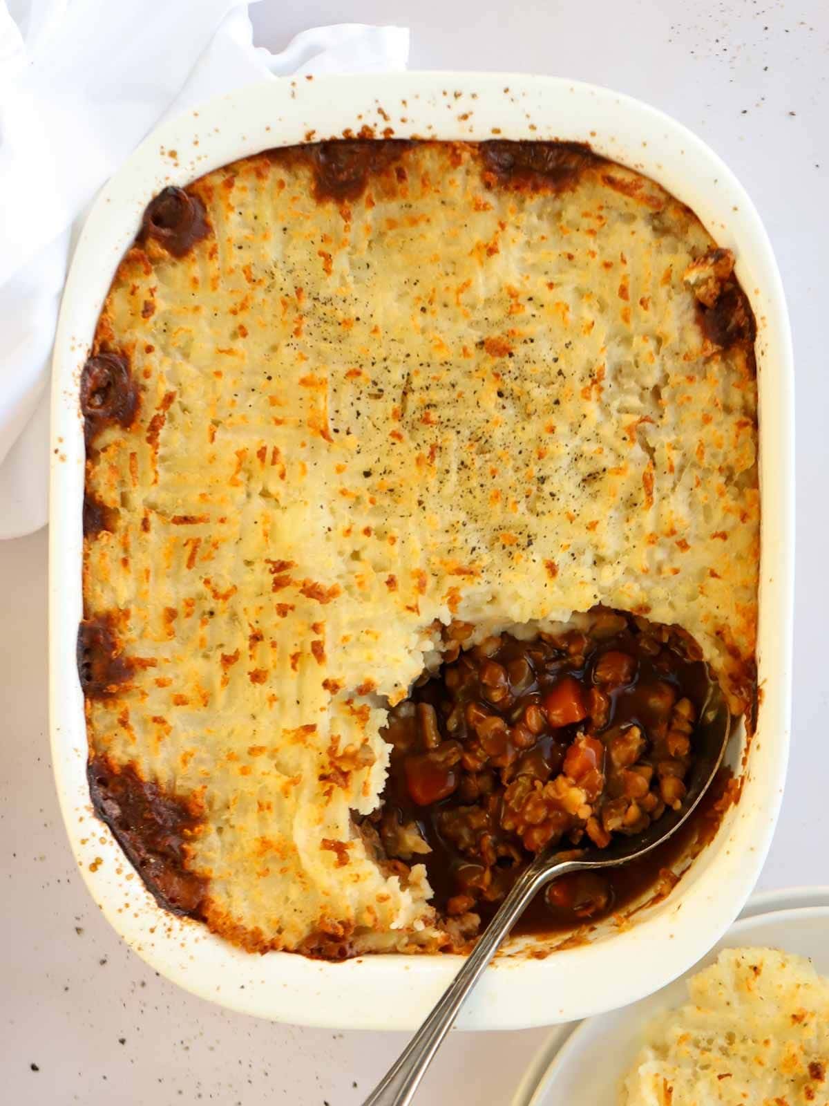 A vegetarian cottage pie straight out of the oven with a golden brown top and a portion already dished out with a spoon.