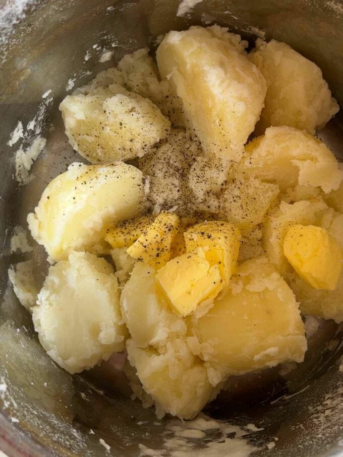 Boiled potatoes in a pan with knobs of butter, ready to be mashed for step 2 in the recipe for Vegetarian Cottage Pie.