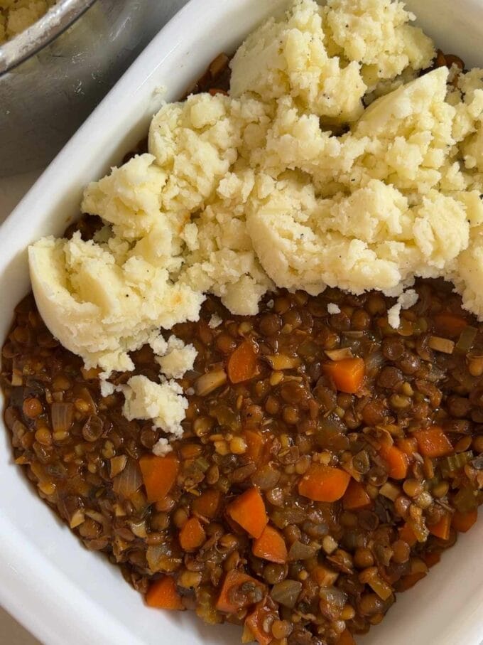 Step 3 in the recipe for Vegetarian Cottage Pie. Mashed potato being added on top of the filling in a dish.