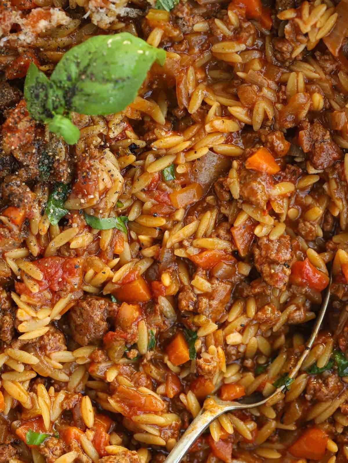 Close up of cooked Orzo Bolognese dish, with tomatoes, beef mince and basil.
