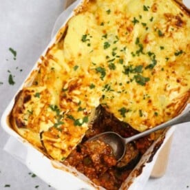 A oven dish filled with rich vegetarian moussaka, with a square missing as it's been served on a plate.