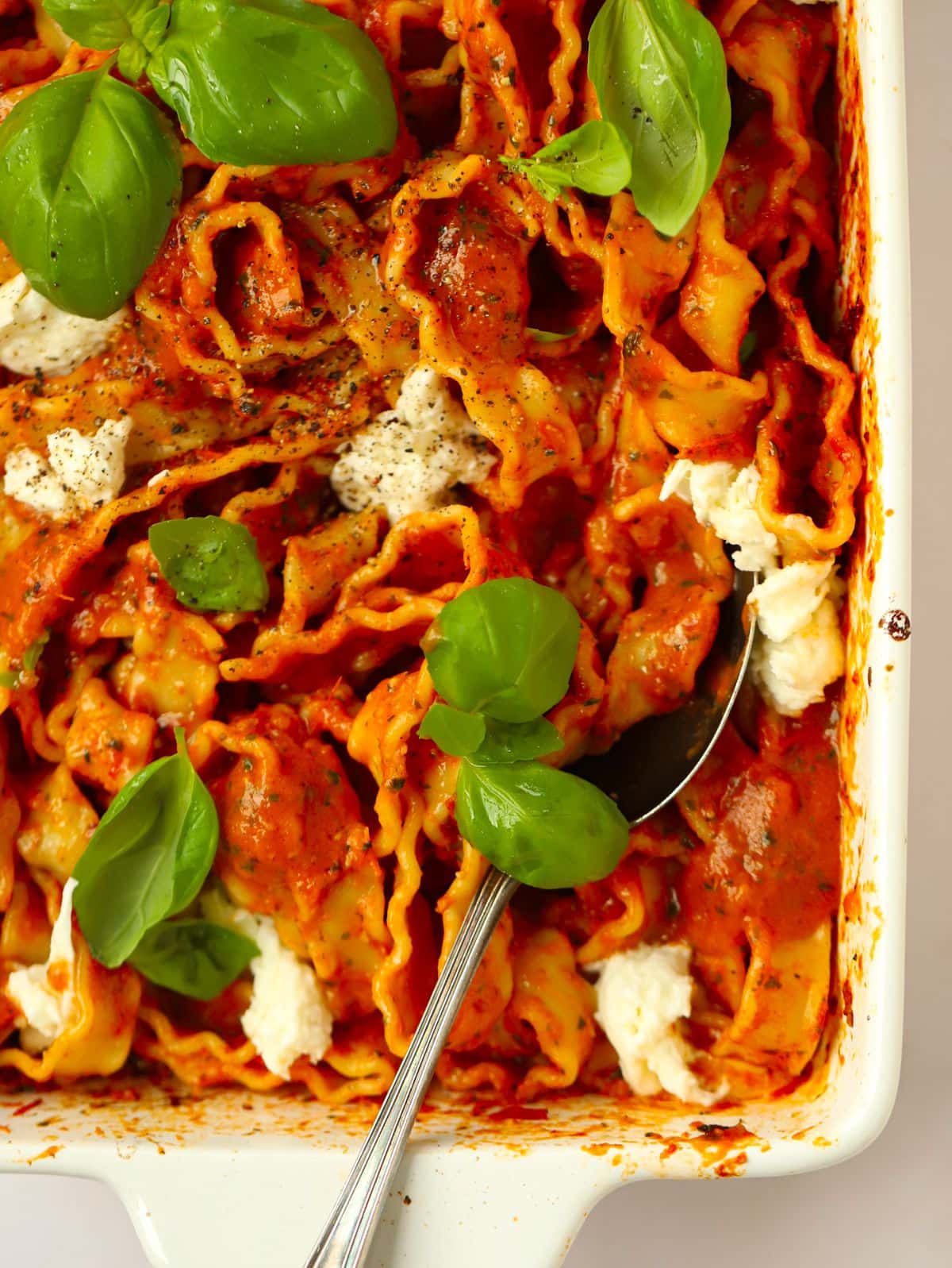A spoon in a big dish filled with cooked Tomato and Basil Pasta, ready to be served.