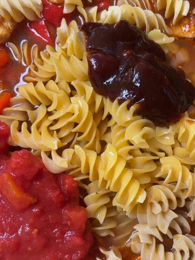 Step 3 in the process for BBQ Chicken Pasta recipe. Add tomatos, flavouring, pasta and barbecue sauce to the pan.