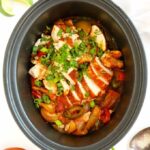 Slow cooker filled with cooked chicken fajitas.
