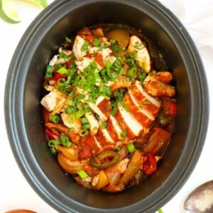 Slow cooker filled with cooked chicken fajitas.