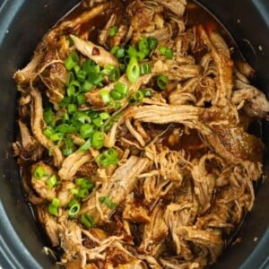 Slow cooker pan filled with cooked pulled pork with chipotle and honey, topped with spring onions.