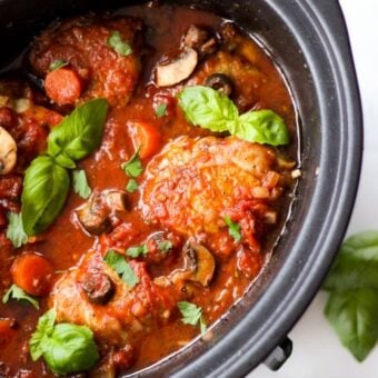A slow cooker filled with cooked chicken in a tomatoey sauce for a delicious Chicken Cacciatore dinner.