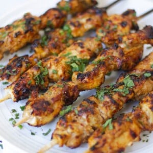 Side photo of chicken kebabs sprinkled with mint. Chicken kebabs lying on a white plate.