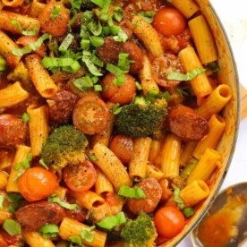 One big pan filled with chorizo pasta with tomato sauce and broccoli.