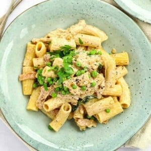 Quick and simple cream cheese pasta on a plate with peas and parsley on top. Ready to serve.