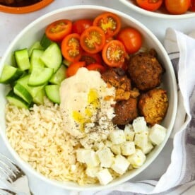 A bowl filled with falafel, tomatoes, cucumber, rice, feta and hummus.