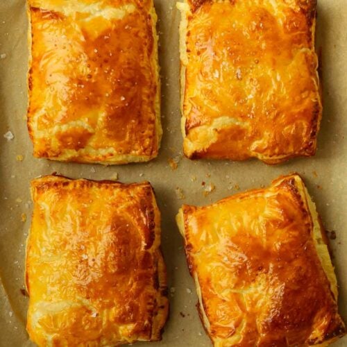 Four cheese and onion pasties with puff pastry on a baking tray.