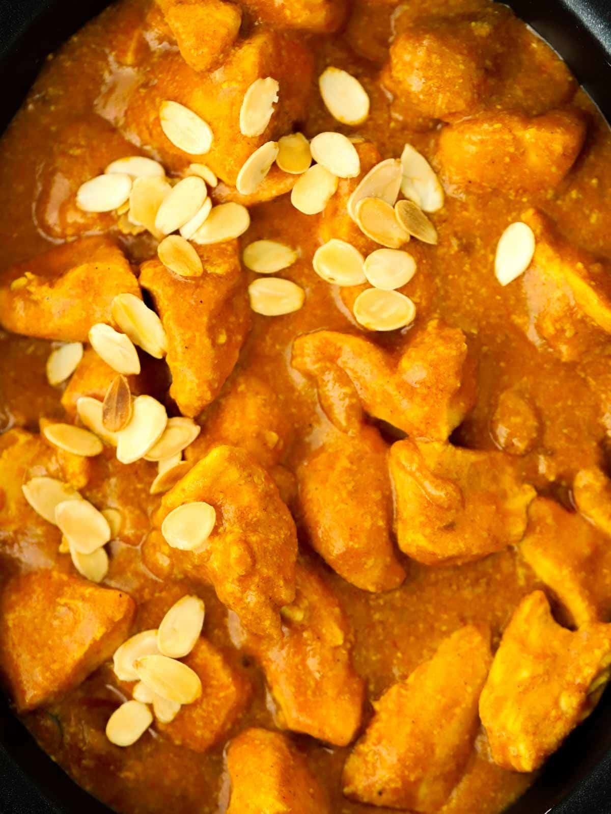 A close up of chicken pieces in a korma curry sauce, topped with almond flakes.