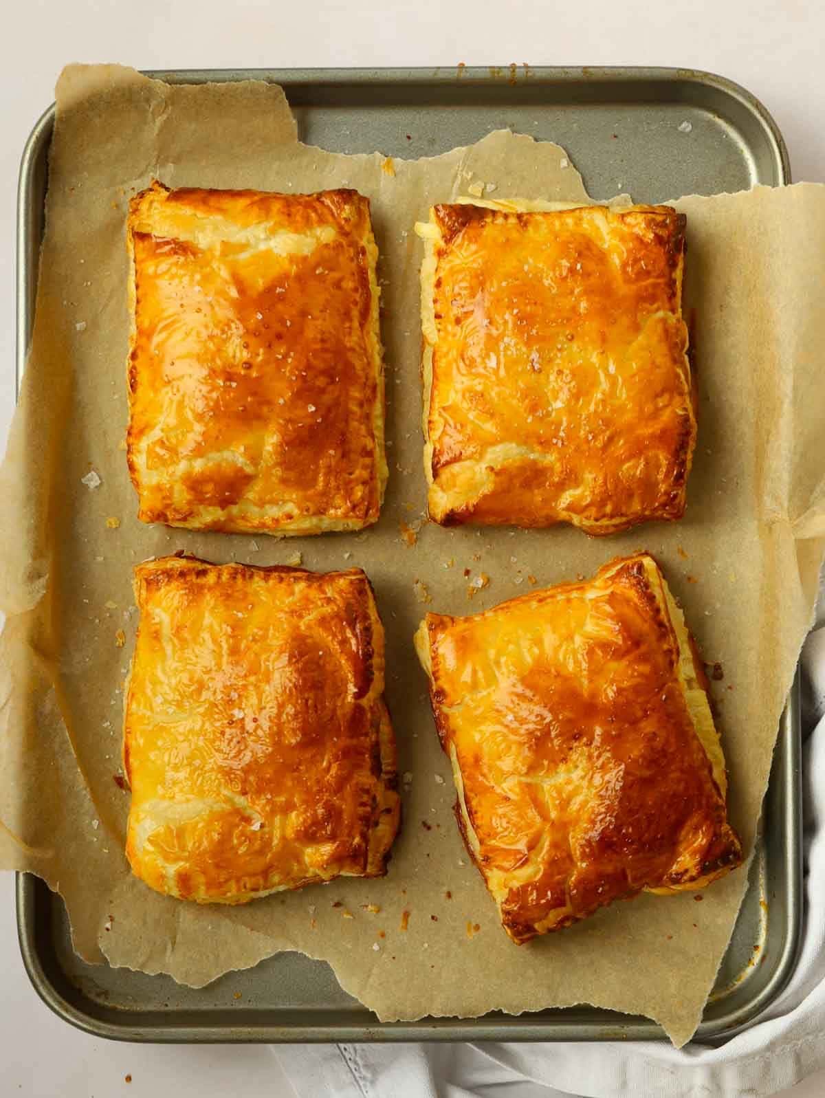 Four cheese and onion pasties on a baking tray straight out of the oven.