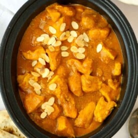 A big slow cooker pan filled with chicken korma curry and topped with almond flakes, ready to be served.