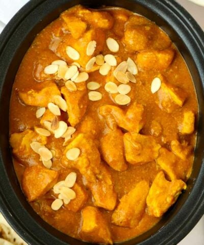 A big slow cooker pan filled with chicken korma curry and topped with almond flakes, ready to be served.
