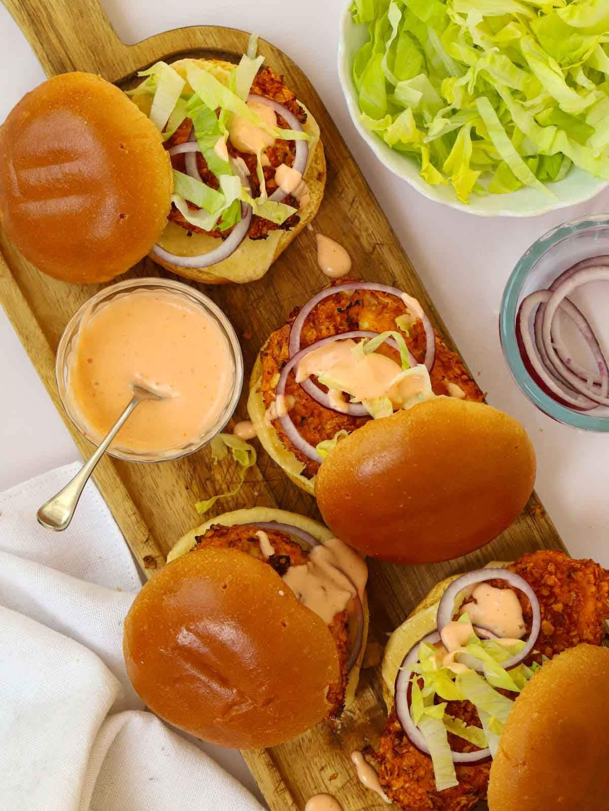 A serving board filled with crispy chicken burgers, hot honey sauce and side salad.