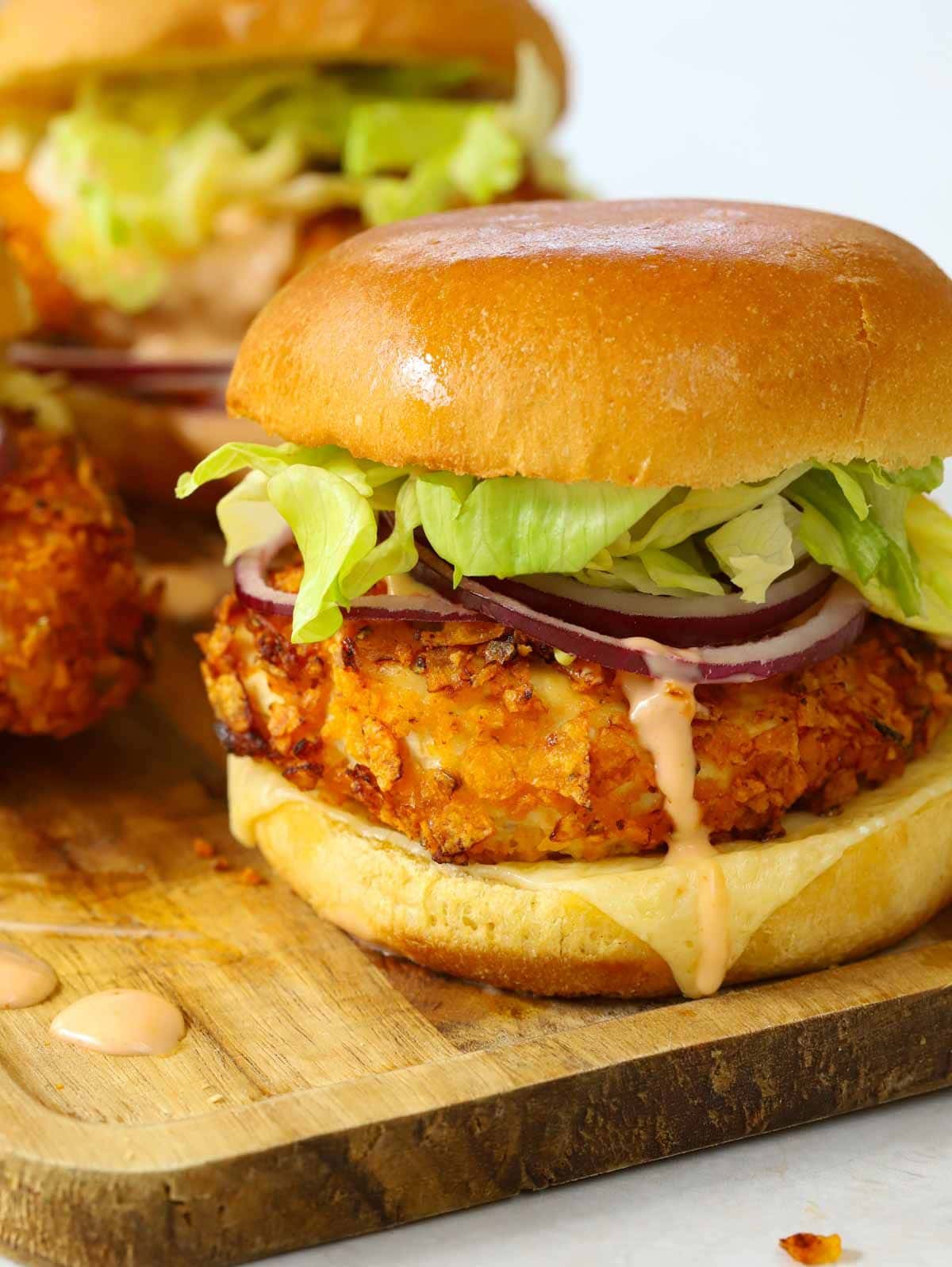 A Crispy Chicken Burger with salad and hot honey sauce on a serving board, ready to eat.