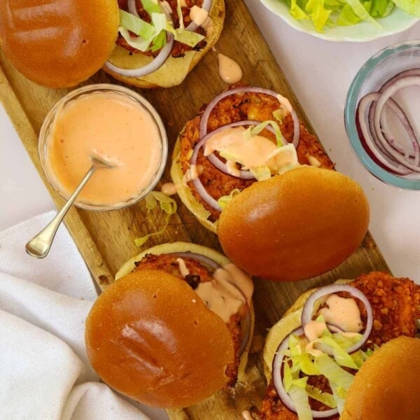Crispy Chicken Burgers on a board with a side of dressing and salad.