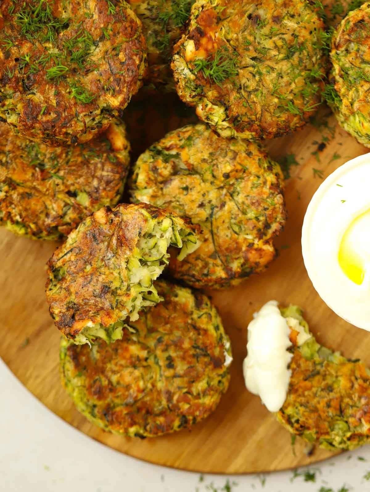 Courgette fritters on a board, with one with a bite missing and another piece dipped in a creamy sauce.