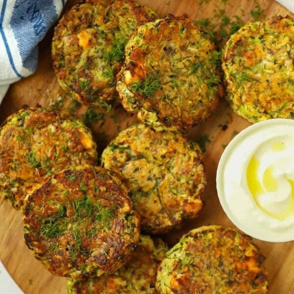 Courgette fritters on a board with a creamy dip.