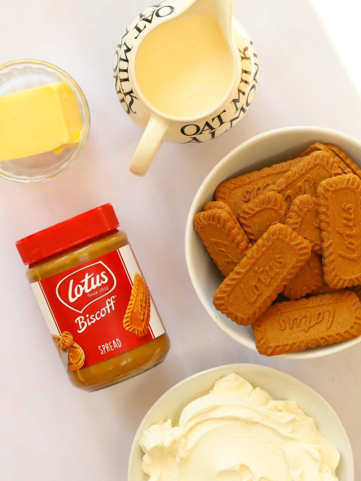 Ingredients for Biscoff Cheesecake laid out on a counter top. Butter, cream, biscuits, Biscoff butter and cream cheese.