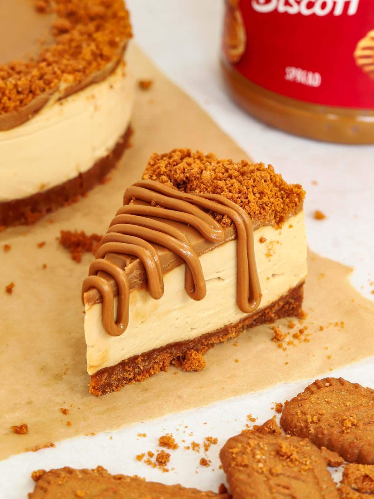 A slice of Biscoff cheesecake on a sheet of baking paper, ready to eat.