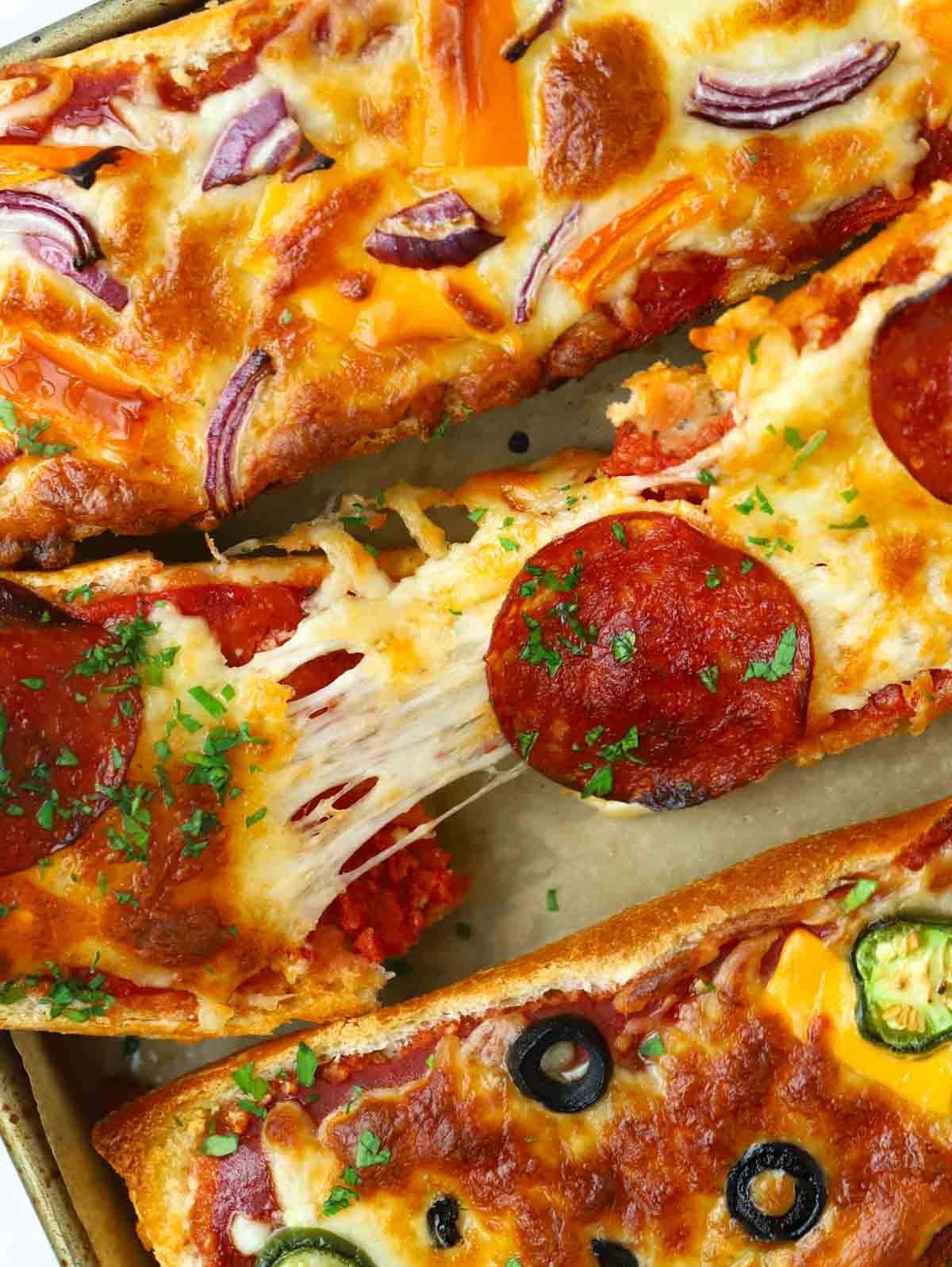 A cooked french bread pizza being torn in half to show stringy cheese.