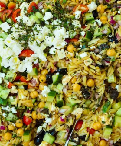 A mixture of orzo pasta and salad ingredients for the recipe Orzo Pasta Salad. Including chickpeas, cheese, cucumber, onion and mint.