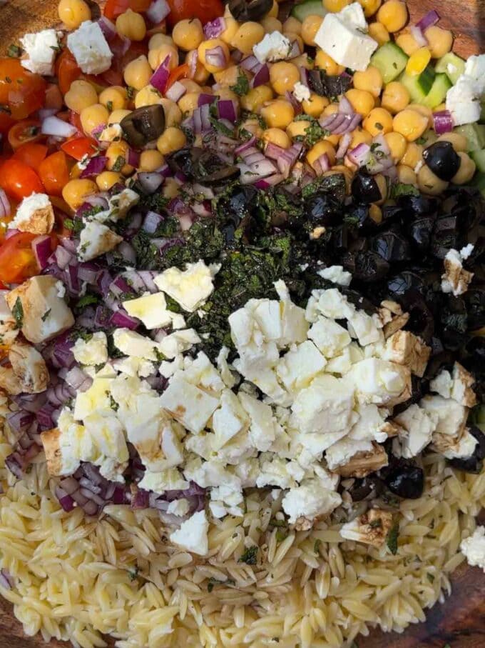 Lots of ingredients for Orzo Pasta Salad in a bowl, ready to be mixed.