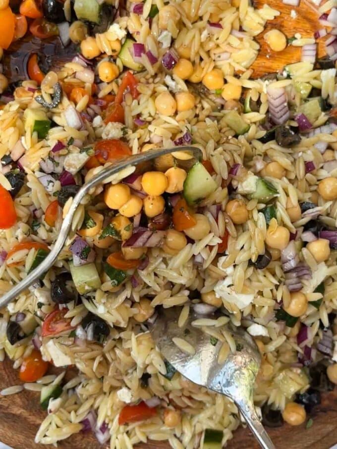 Two spoons mixing up all of the ingredients for Orzo Pasta Salad.