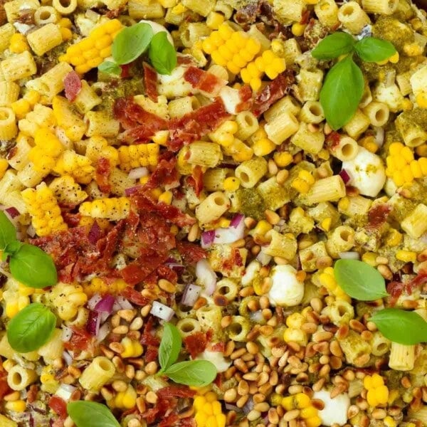 A close up of pasta mixed together with lots of ingredients to make a delicious pesto pasta salad.